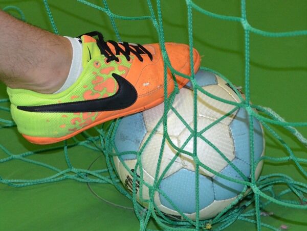 Ein Sportschuh berührt einen Fußball im Tornetz