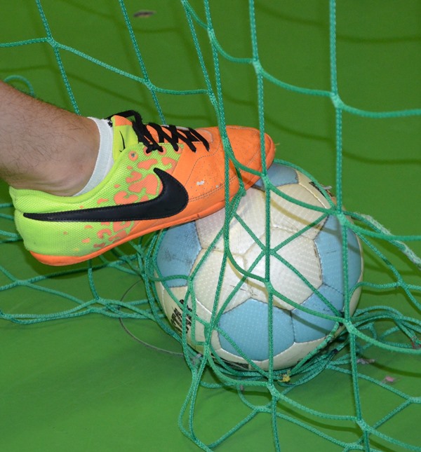 Ein Sportschuh berührt einen Fußball im Tornetz