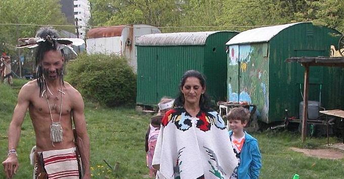 Indianer stehen um ein Feuer, im Hinbtergrund Bauwägen