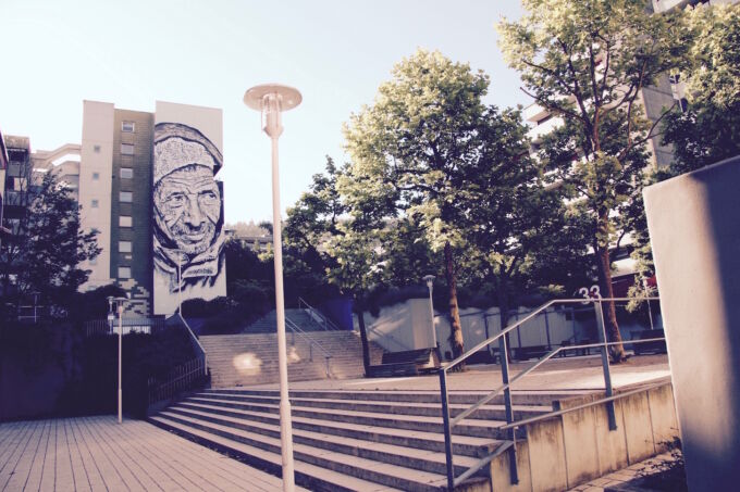 Eine breite Treppe führt zu einem Gebäude auf dem die Malerei eines Mannes großflächig über die ganze Wand zu sehen ist.