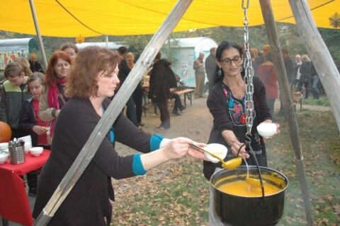 Frauen schöpfen Kürbisfarbene Suppe aus einem großen hängendem Topf